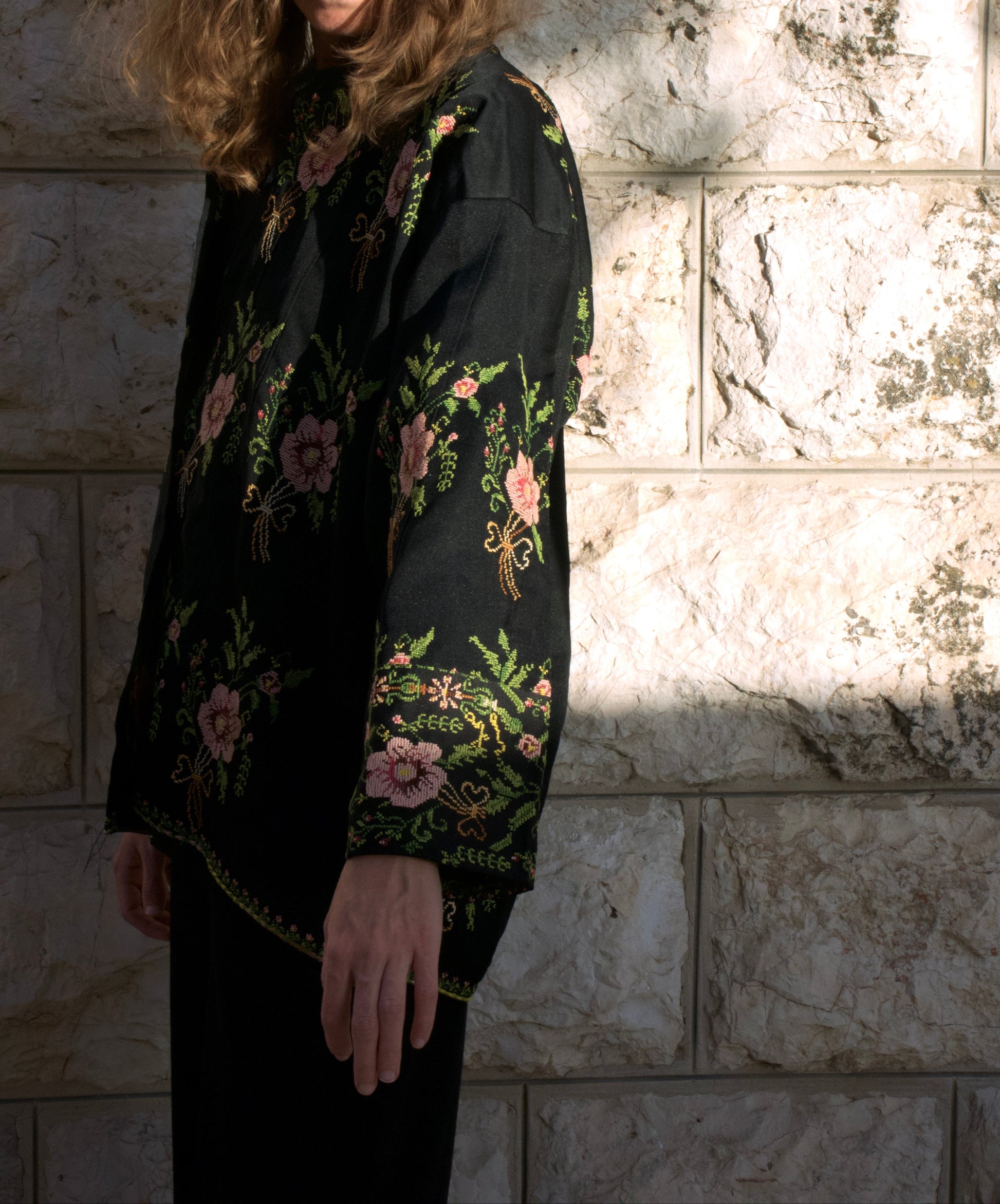 Woman wearing a black floral blouse against a stone wall.
