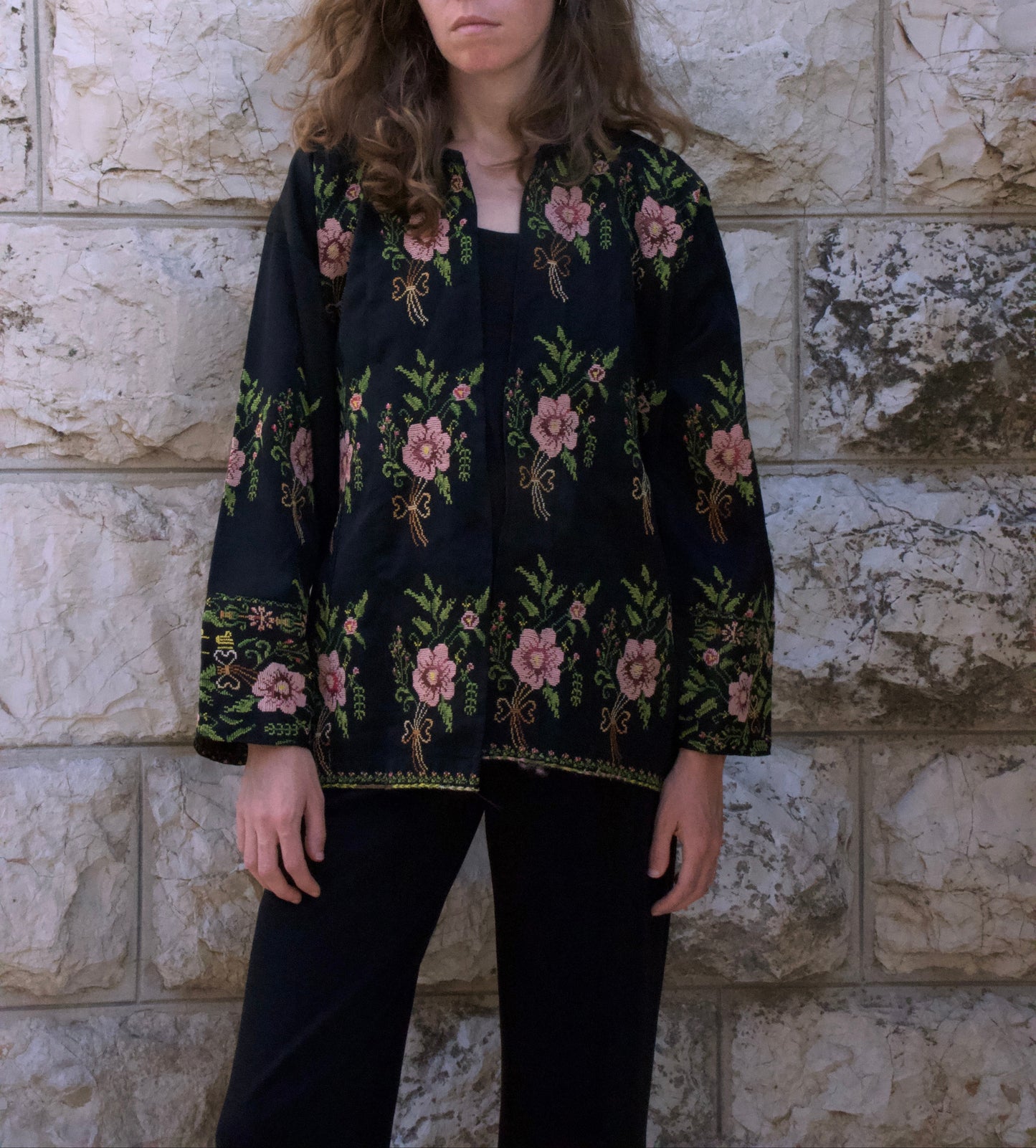 Person wearing a black floral-patterned jacket against a stone wall.