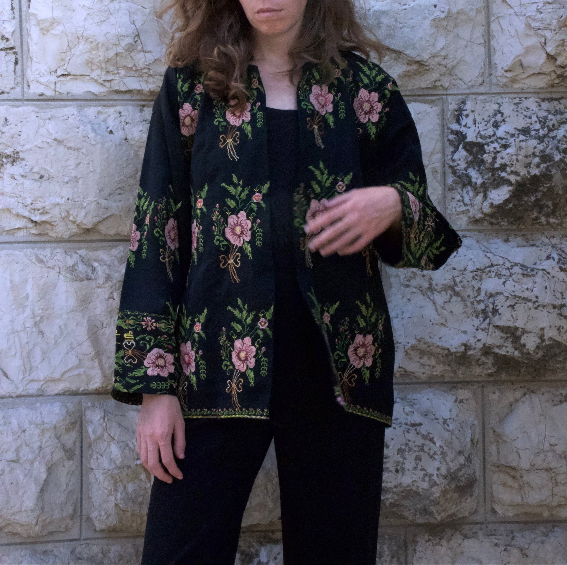 Woman wearing a black floral jacket against a stone wall.