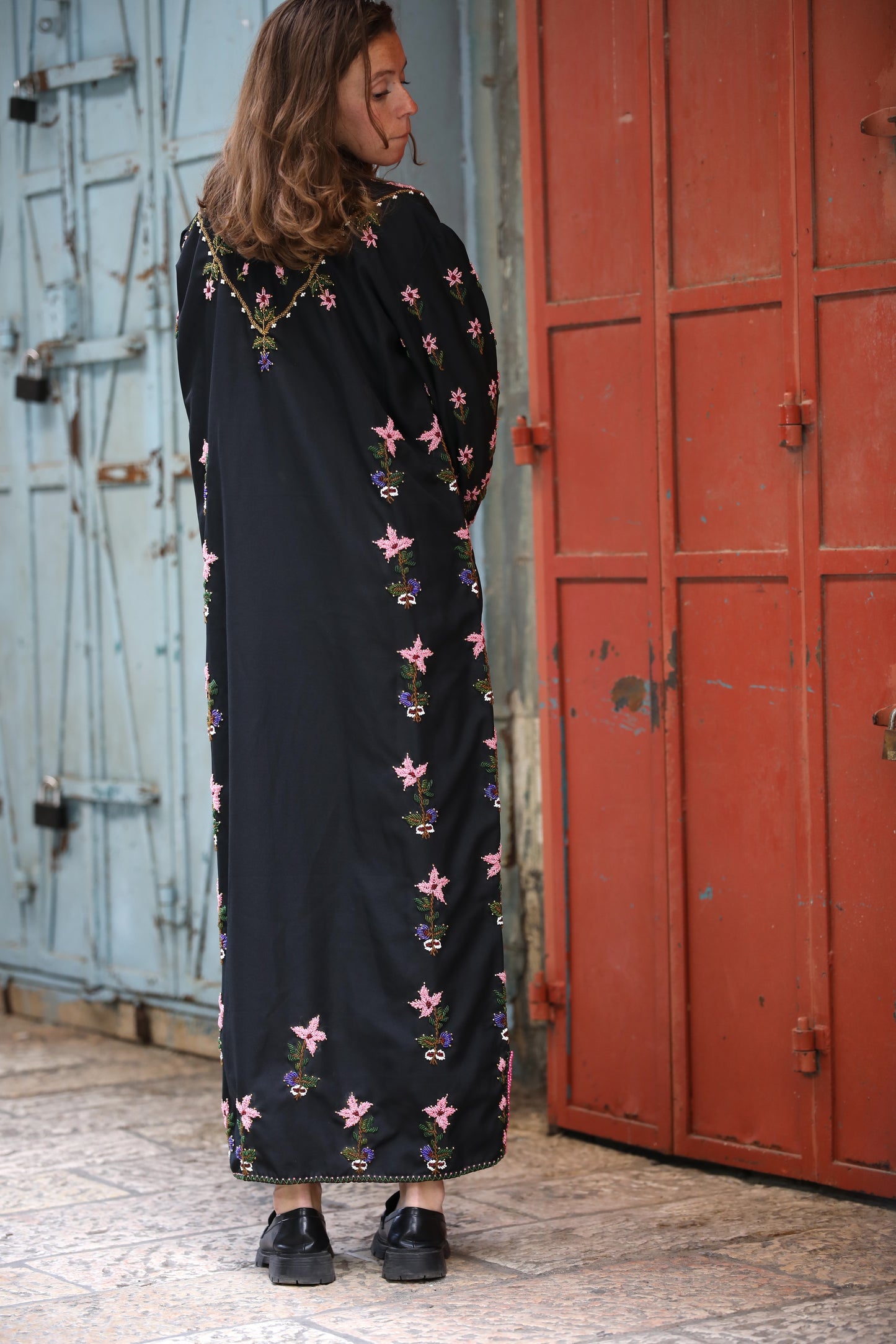 Woman wearing a black dress with floral patterns standing in front of a red door.