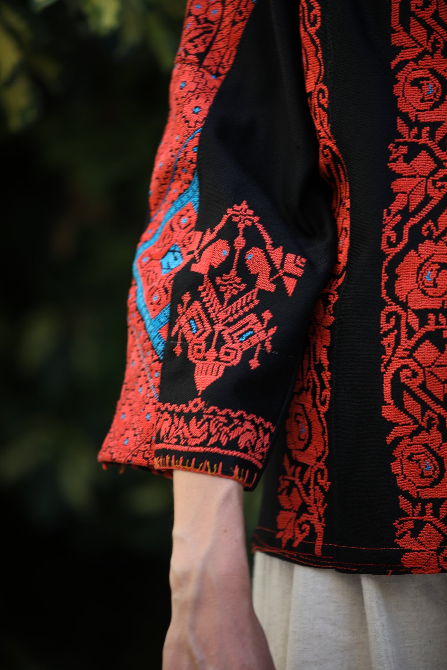 Close-up of a black garment with red embroidery against a blurred green background