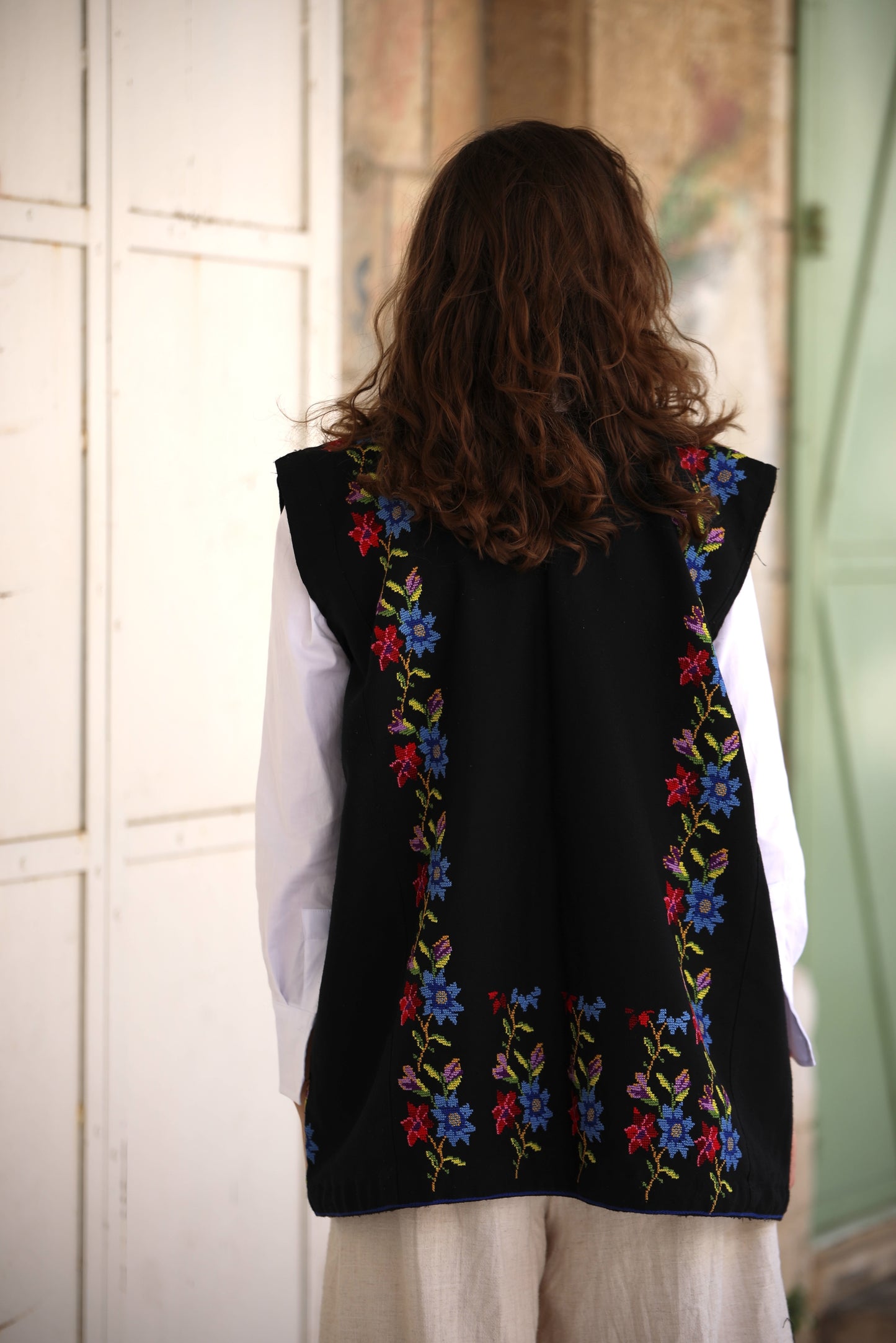 Person wearing a black vest with colorful floral embroidery in a room.