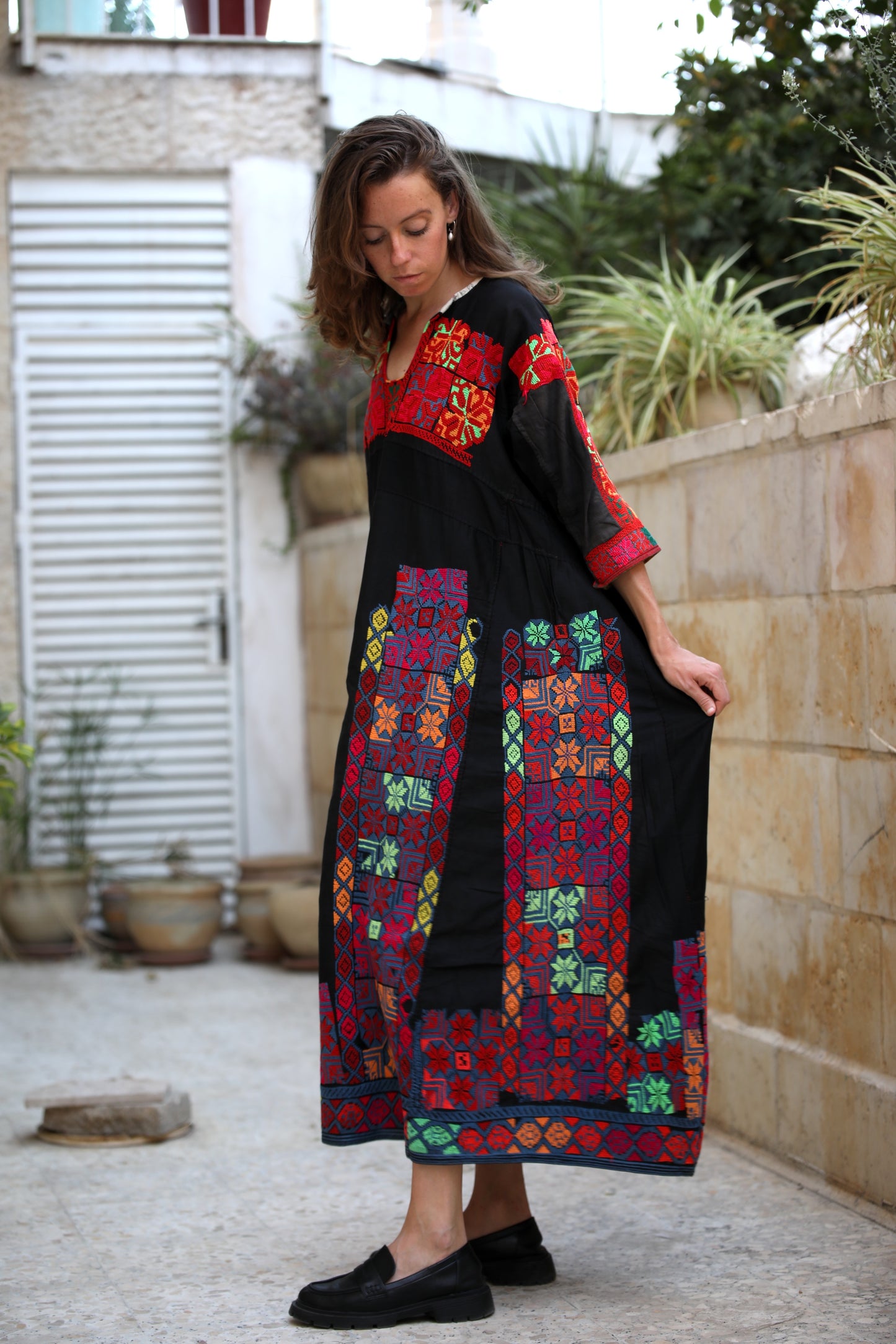 Woman wearing a colorful embroidered dress standing outdoors.