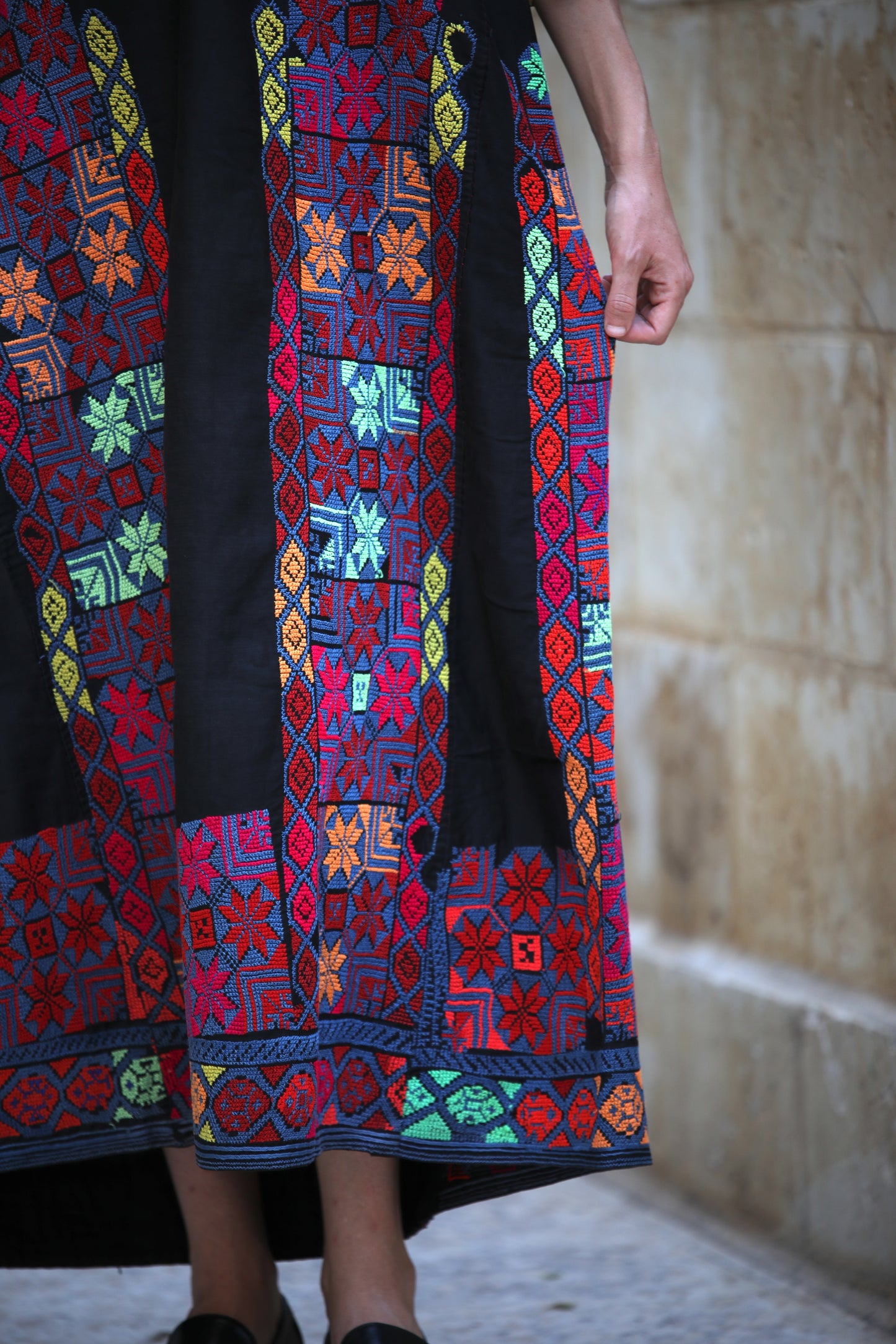 Colorful hand-embroidered dress with geometric patterns on a textured wall background