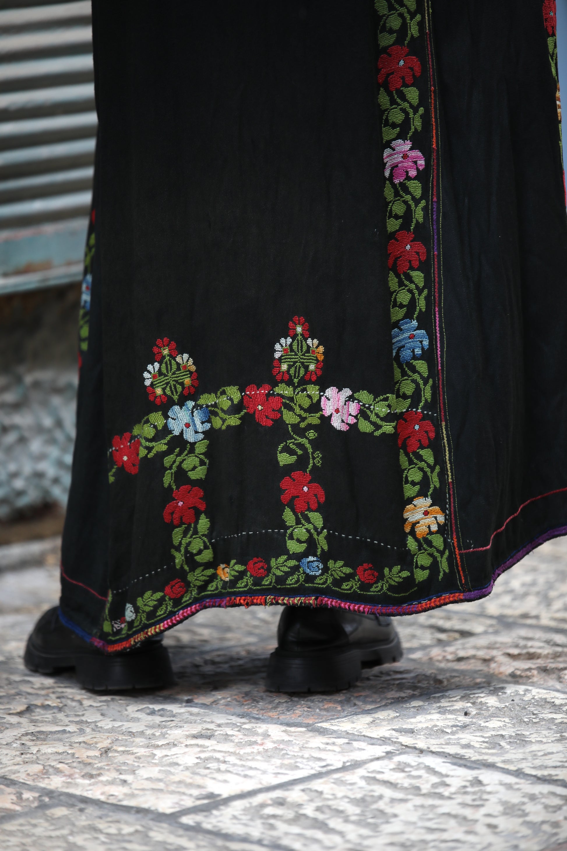 Black dress with colorful floral embroidery on a textured floor.
