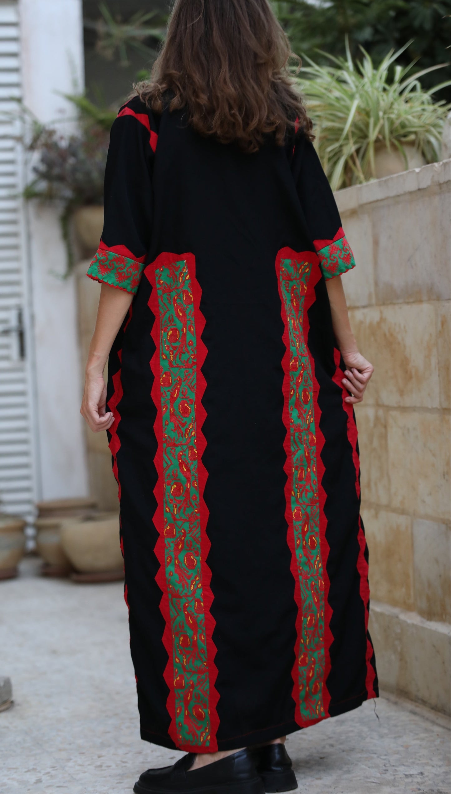 Person wearing a black dress with red and green patterns in an outdoor setting.