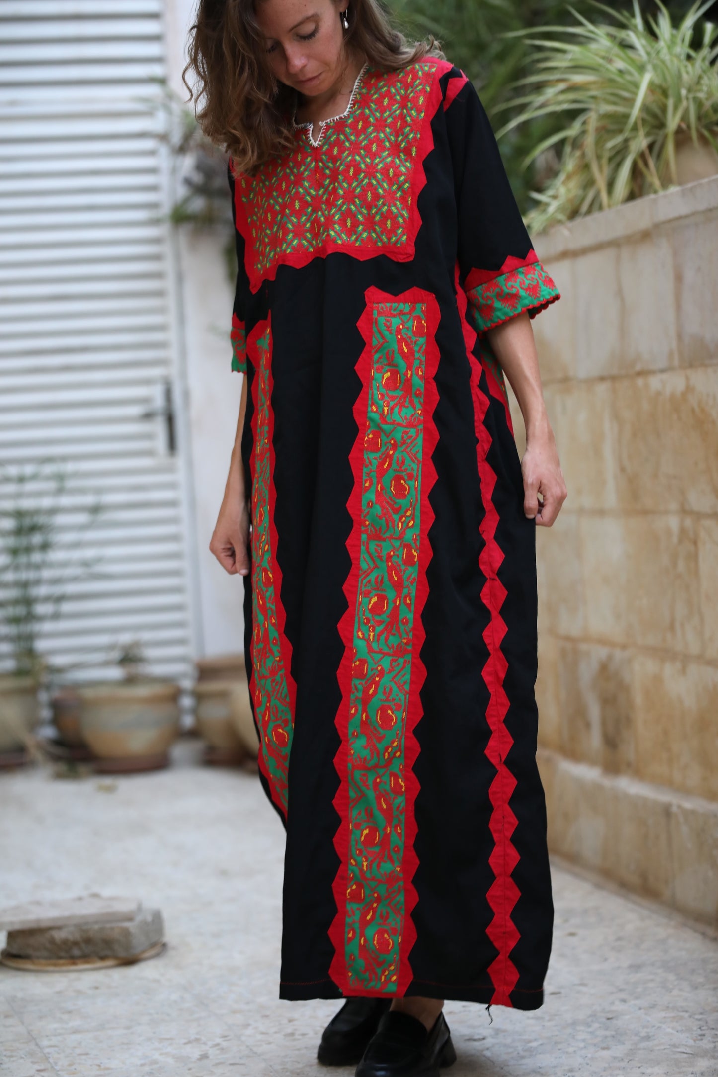 Woman wearing a black dress with red and green embroidery in an outdoor setting.