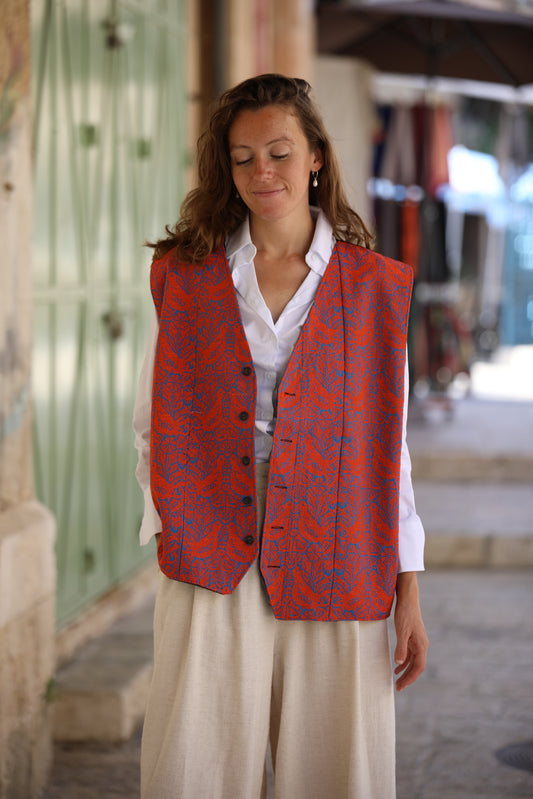 Woman wearing an orange patterned vest over a white shirt in an outdoor setting