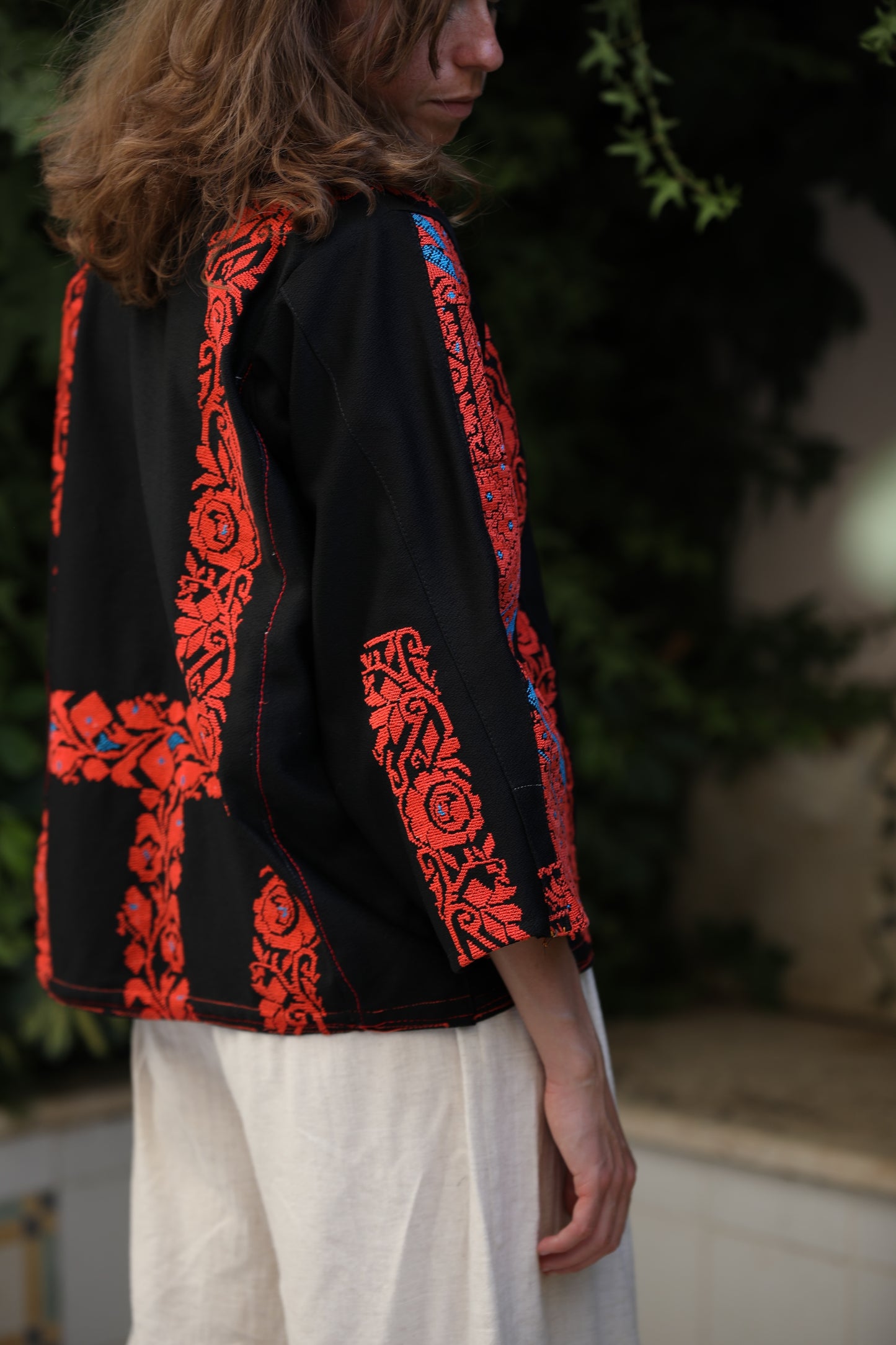 Person wearing a black jacket with red and orange embroidery, standing outdoors.