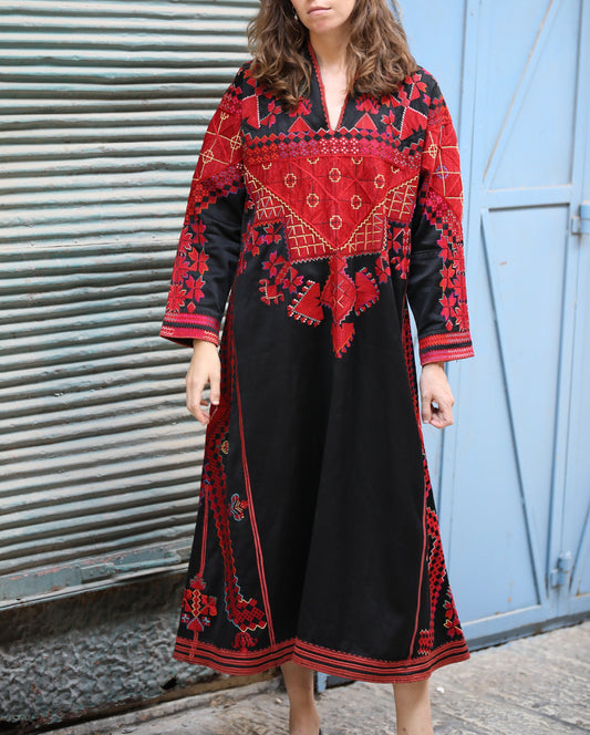 Woman wearing a red and black embroidered dress standing in front of a blue door.