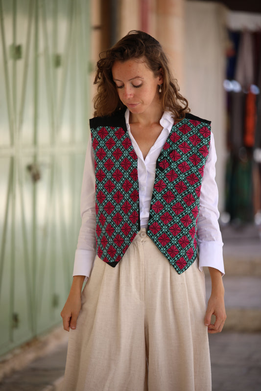 Woman wearing a patterned vest over a white shirt and beige pants in an outdoor setting.