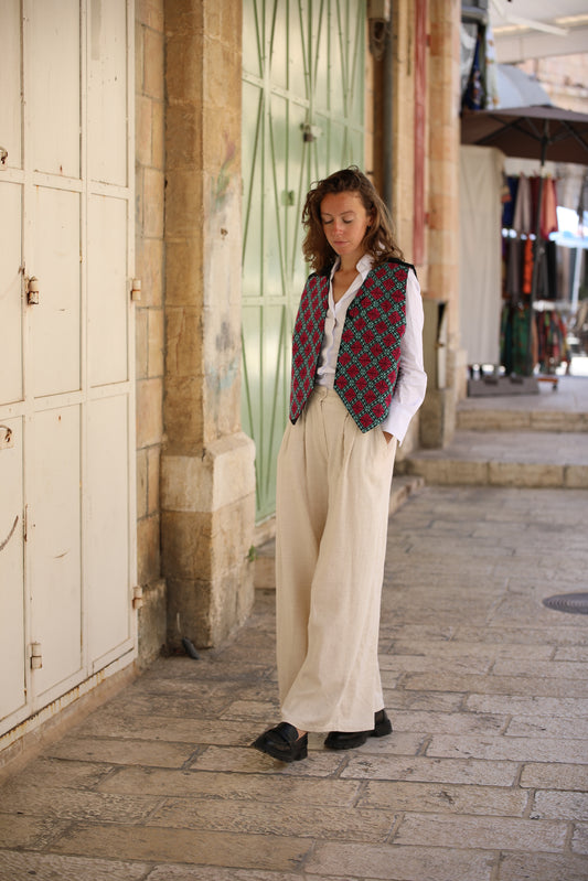 Woman in a plaid vest and white pants standing on a stone pavement.