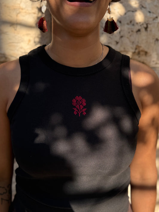 Person wearing a black sleeveless top with a red floral design, standing against a neutral background.