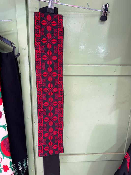 Red patterned belt on a white surface with a metallic object in the background