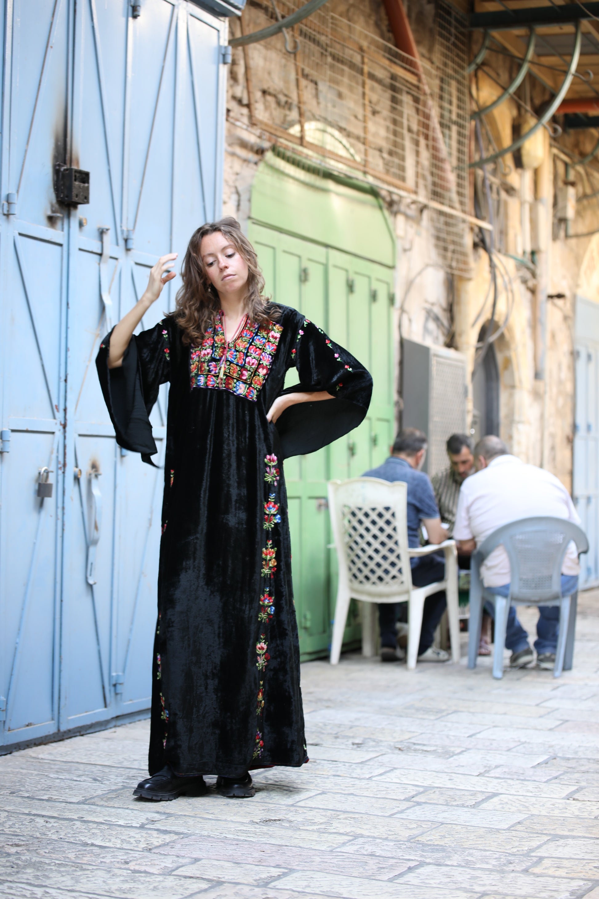 Woman in a black dress with colorful embroidery standing in an outdoor setting.