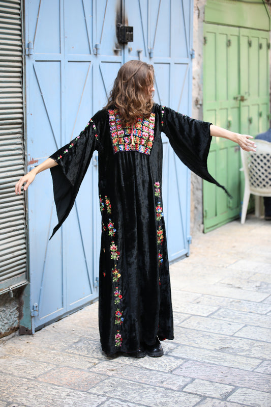 Woman wearing a black dress with colorful embroidery standing in front of blue doors.