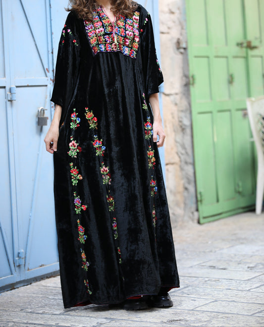 Person wearing a black dress with colorful floral embroidery in an outdoor setting.