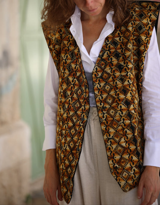 Woman wearing a patterned vest over a white shirt and light pants.