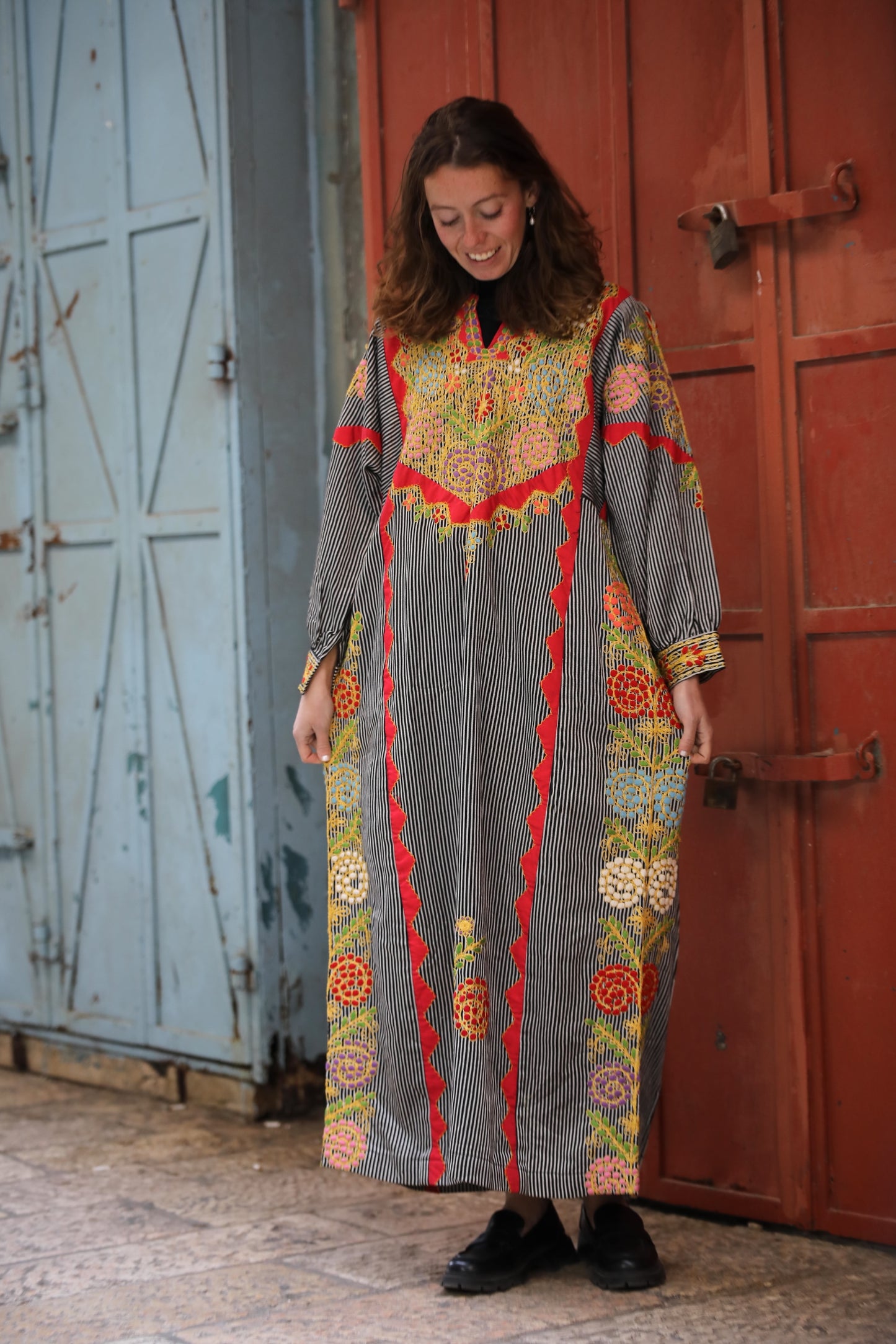 Woman wearing a colorful patterned dress standing in front of a red door.
