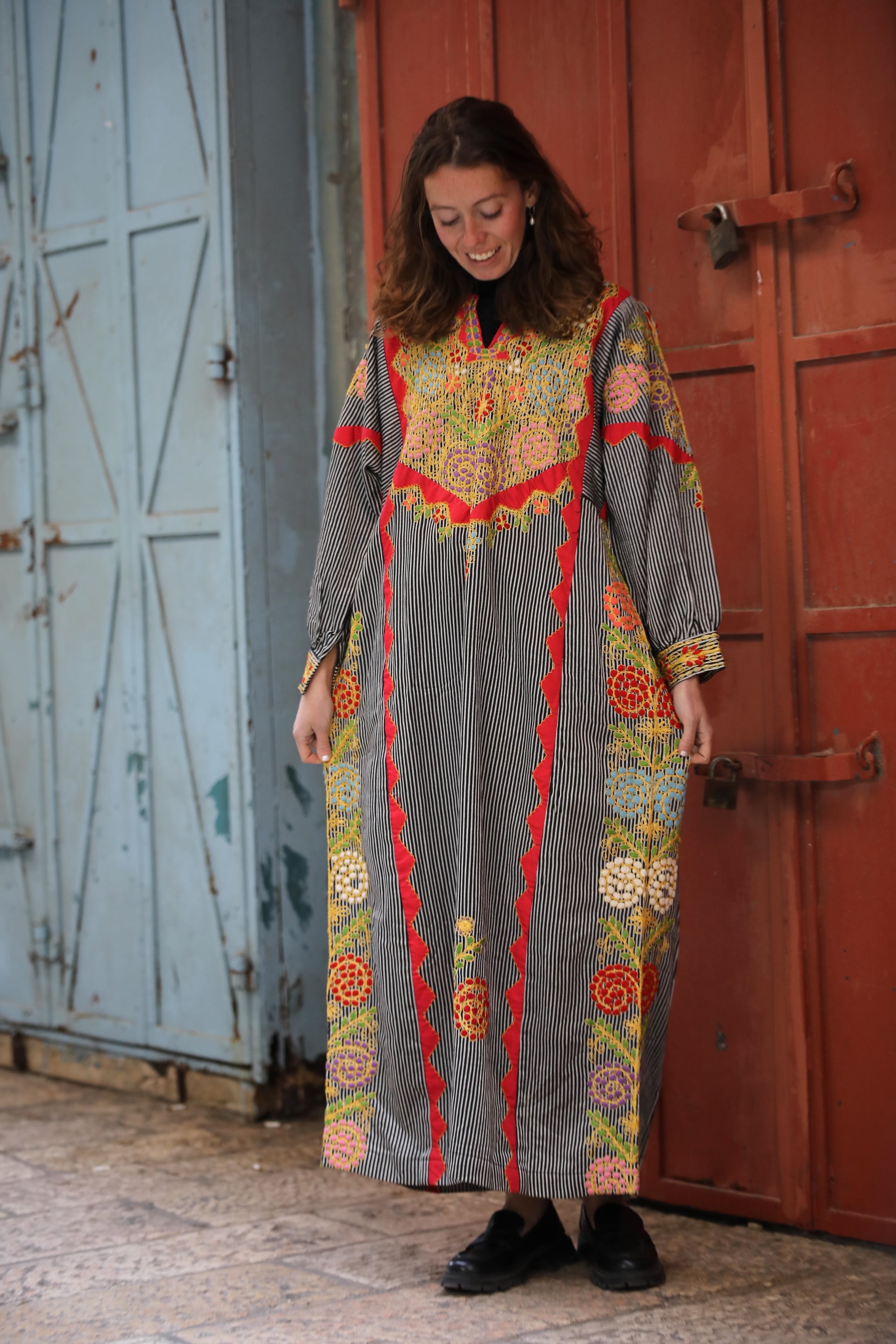 Woman wearing a colorful patterned dress standing in front of a red door.