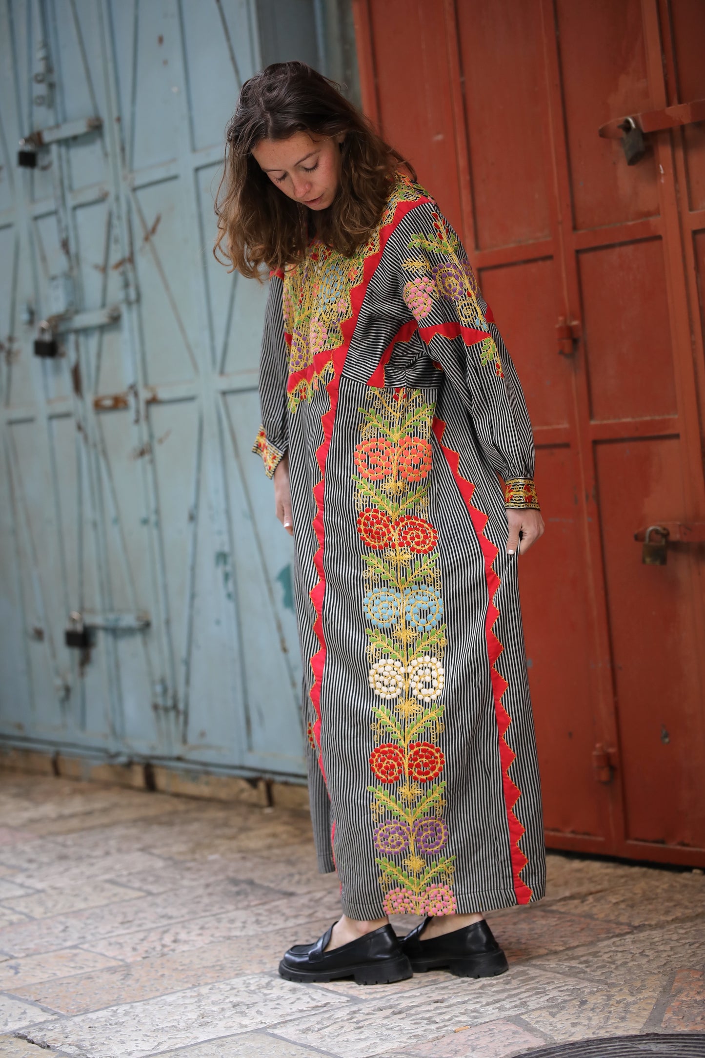 Woman wearing a long, patterned dress standing in front of a rustic door.