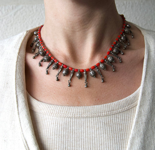 Necklace with red beads and silver pendants on a person wearing a white top.