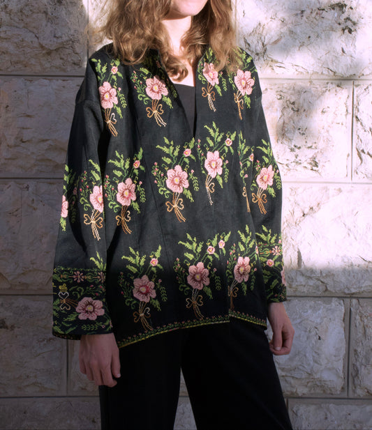 Person wearing a black floral blouse against a stone wall.