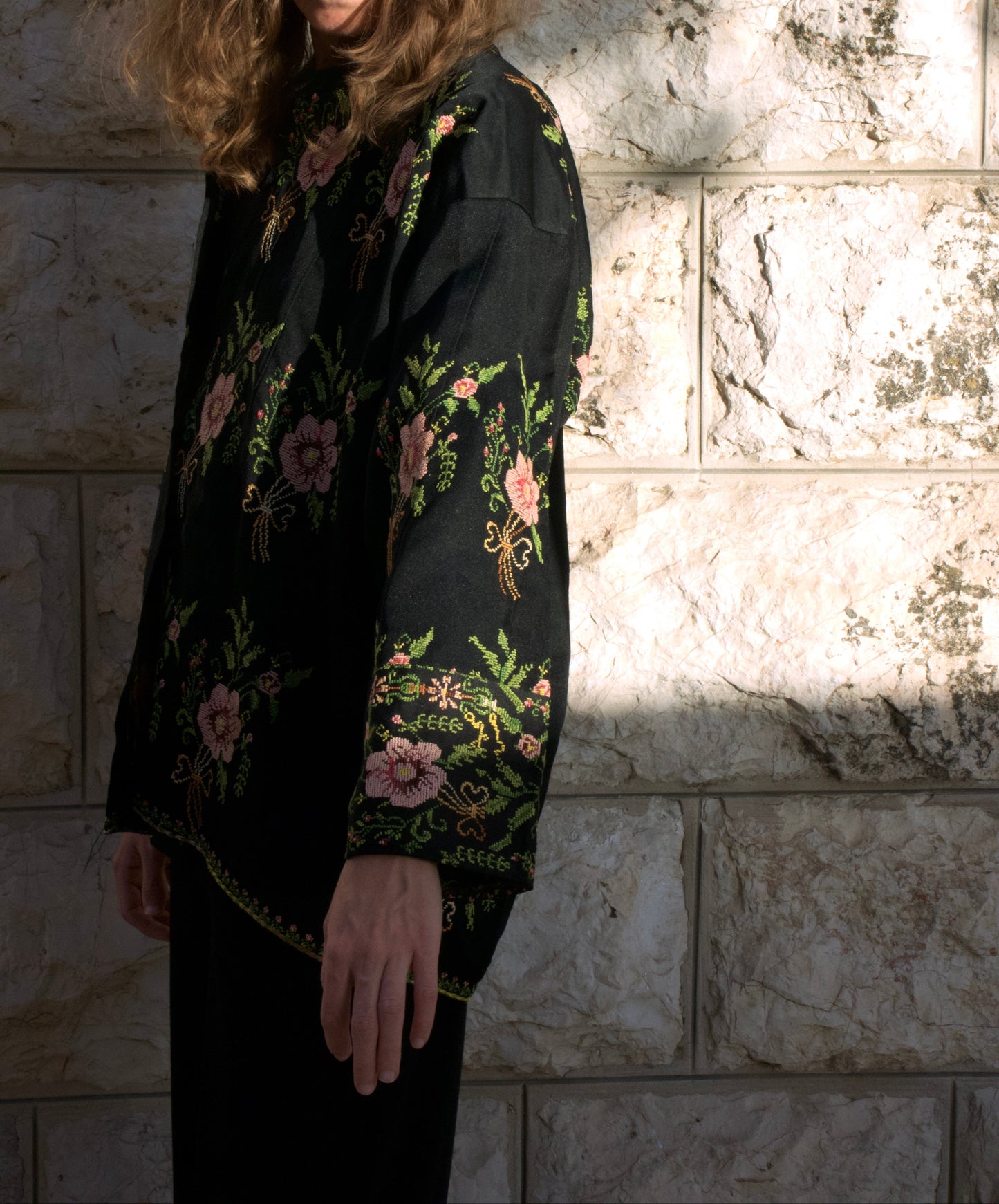 Woman wearing a black floral blouse against a stone wall.