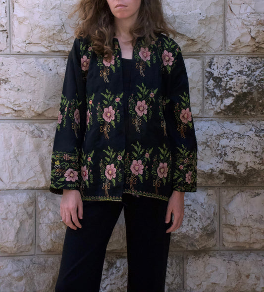 Person wearing a black floral-patterned jacket against a stone wall.