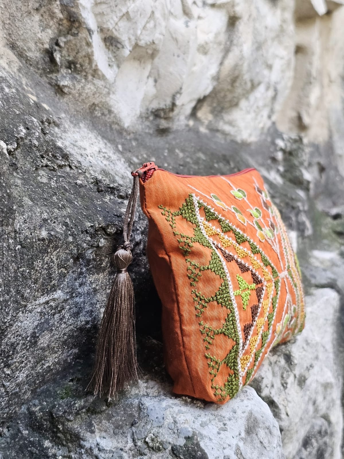 Decorative orange purse with green patterns and a tassel on a stone surface