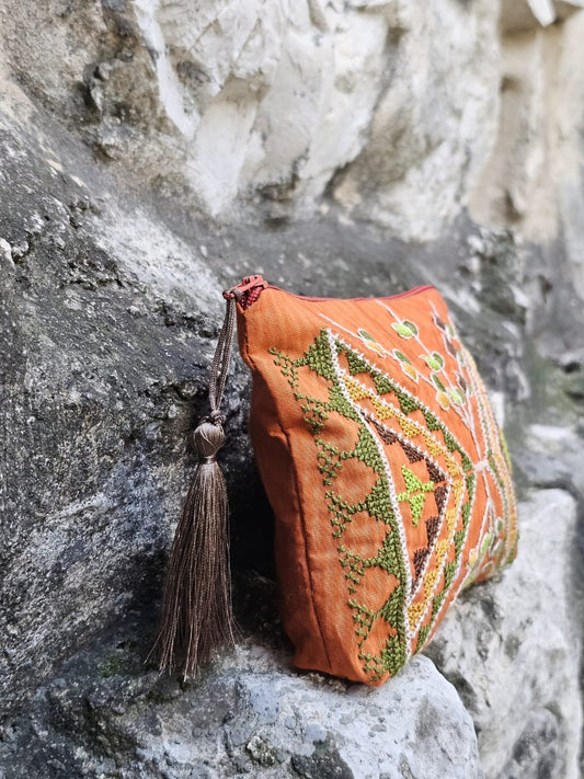 Decorative orange purse with green patterns and a tassel on a stone surface