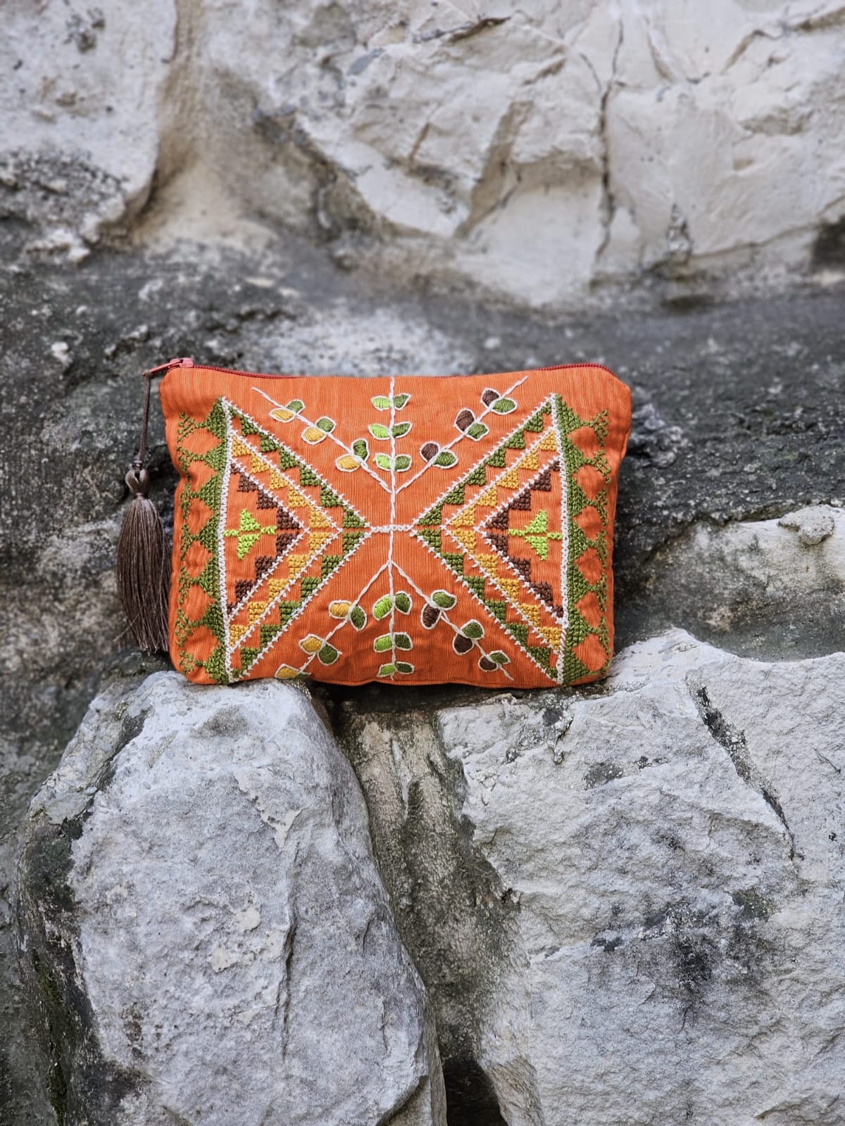 Orange embroidered clutch bag on a rocky surface