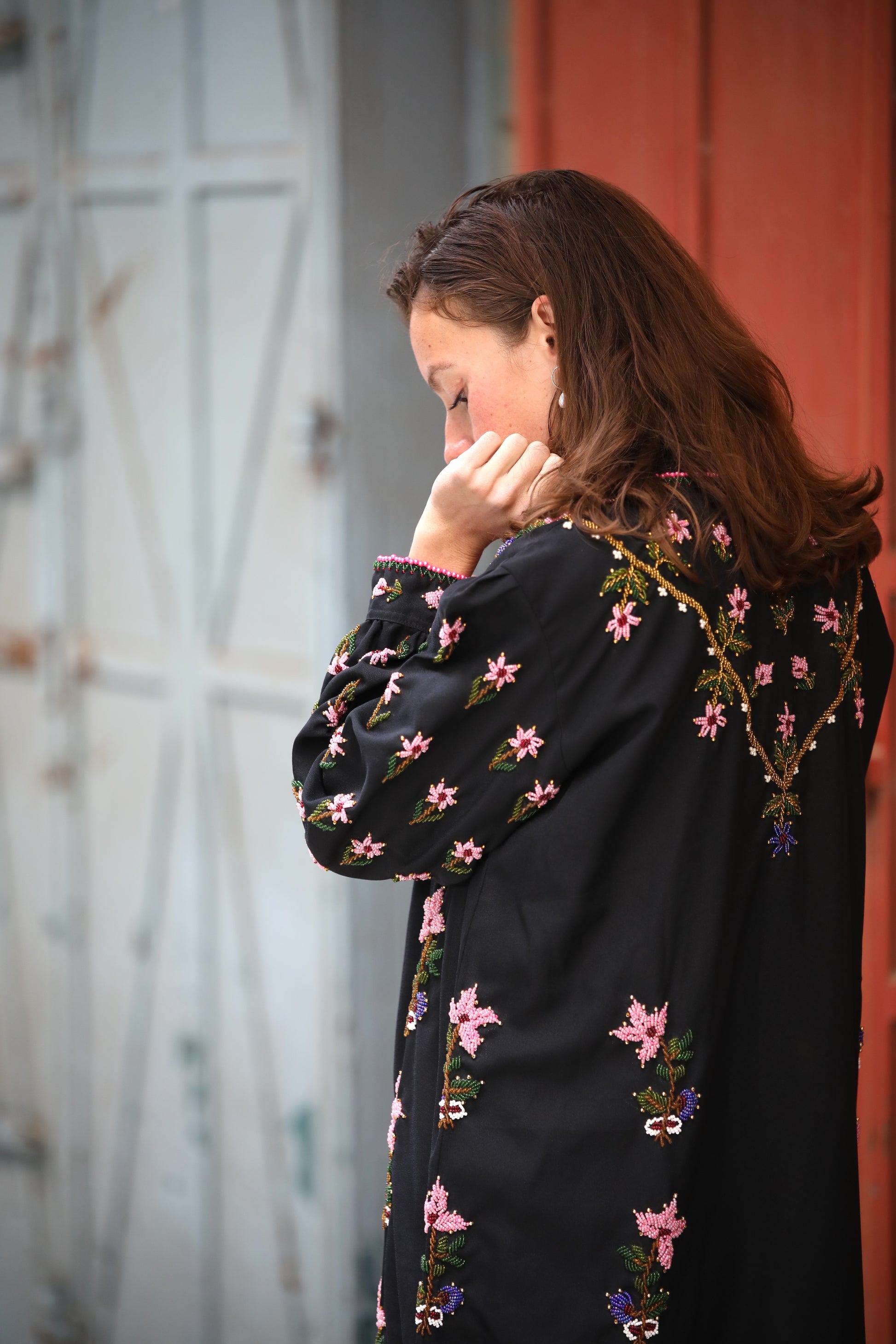 Woman wearing a black embroidered jacket with pink flowers against a blurred background