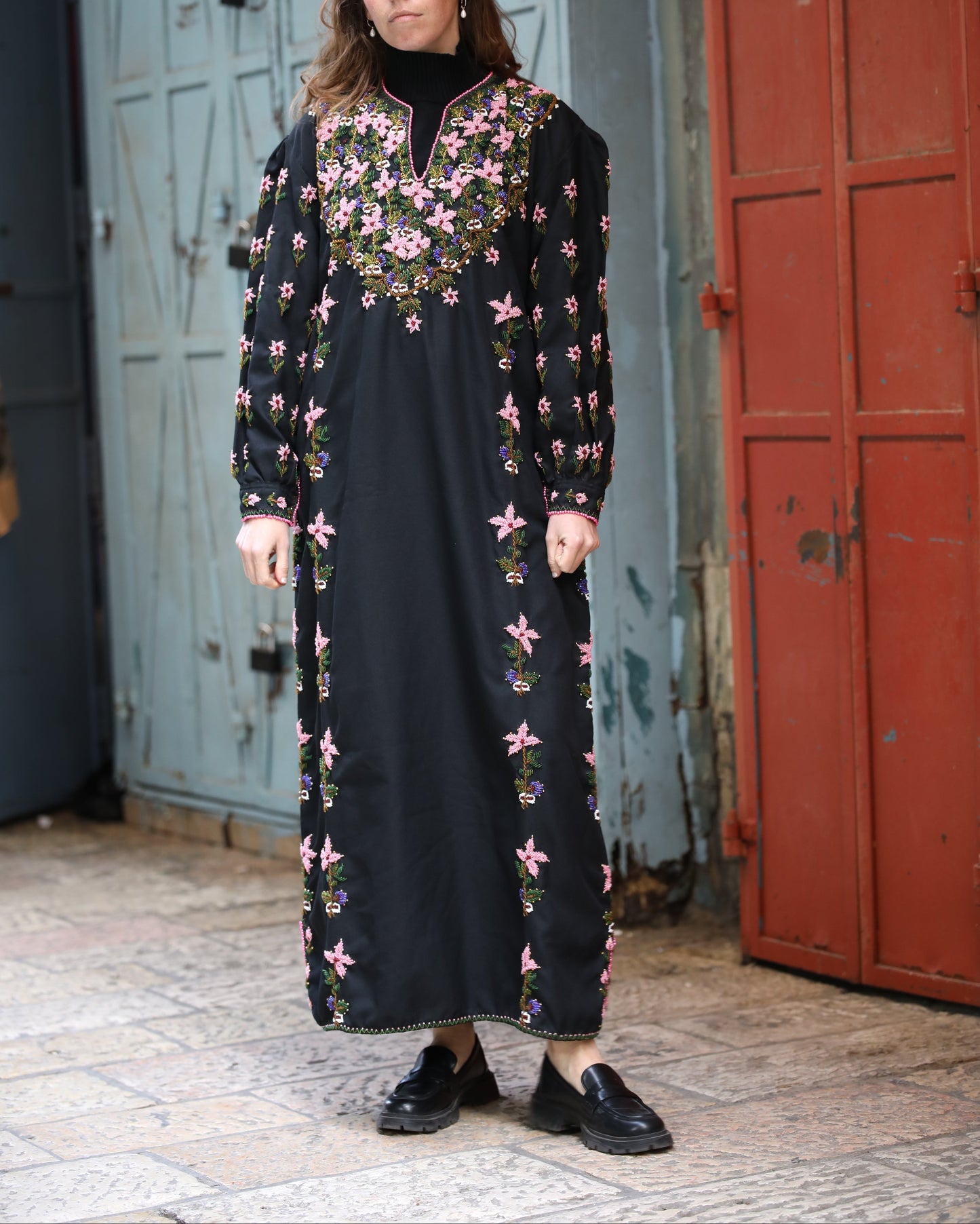 Woman wearing a black dress with floral embroidery standing in front of a textured wall.