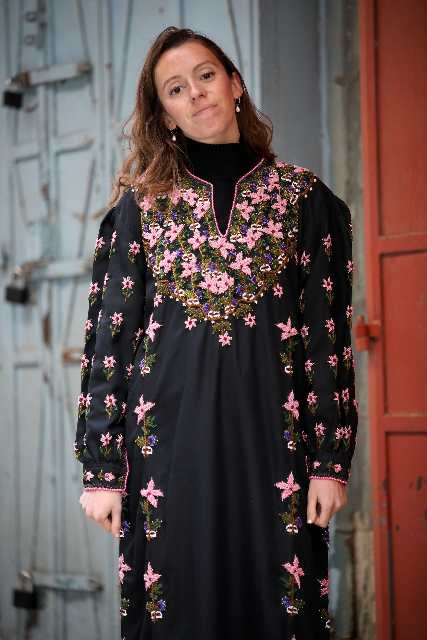 Woman wearing a black dress with pink floral embroidery in a rustic setting.