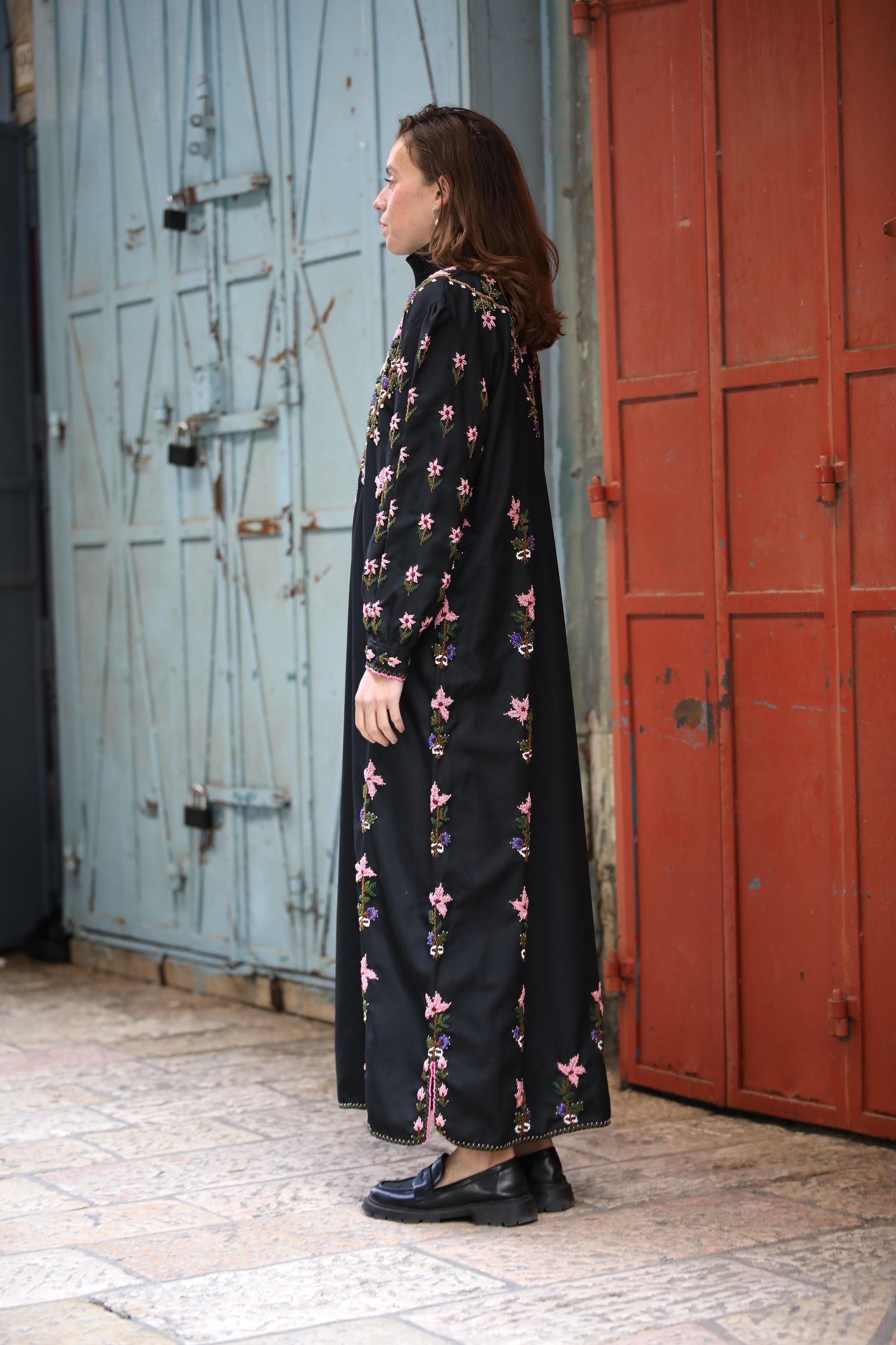 Woman wearing a long black floral dress standing in front of a red and blue door.