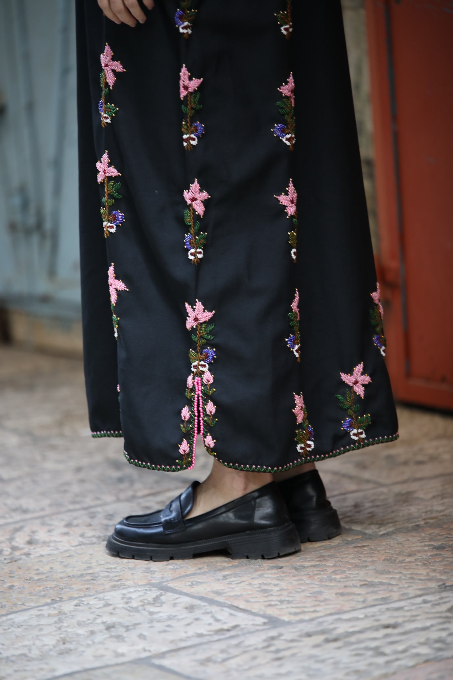 Black embroidered skirt with colorful patterns worn by a person on a stone pavement.