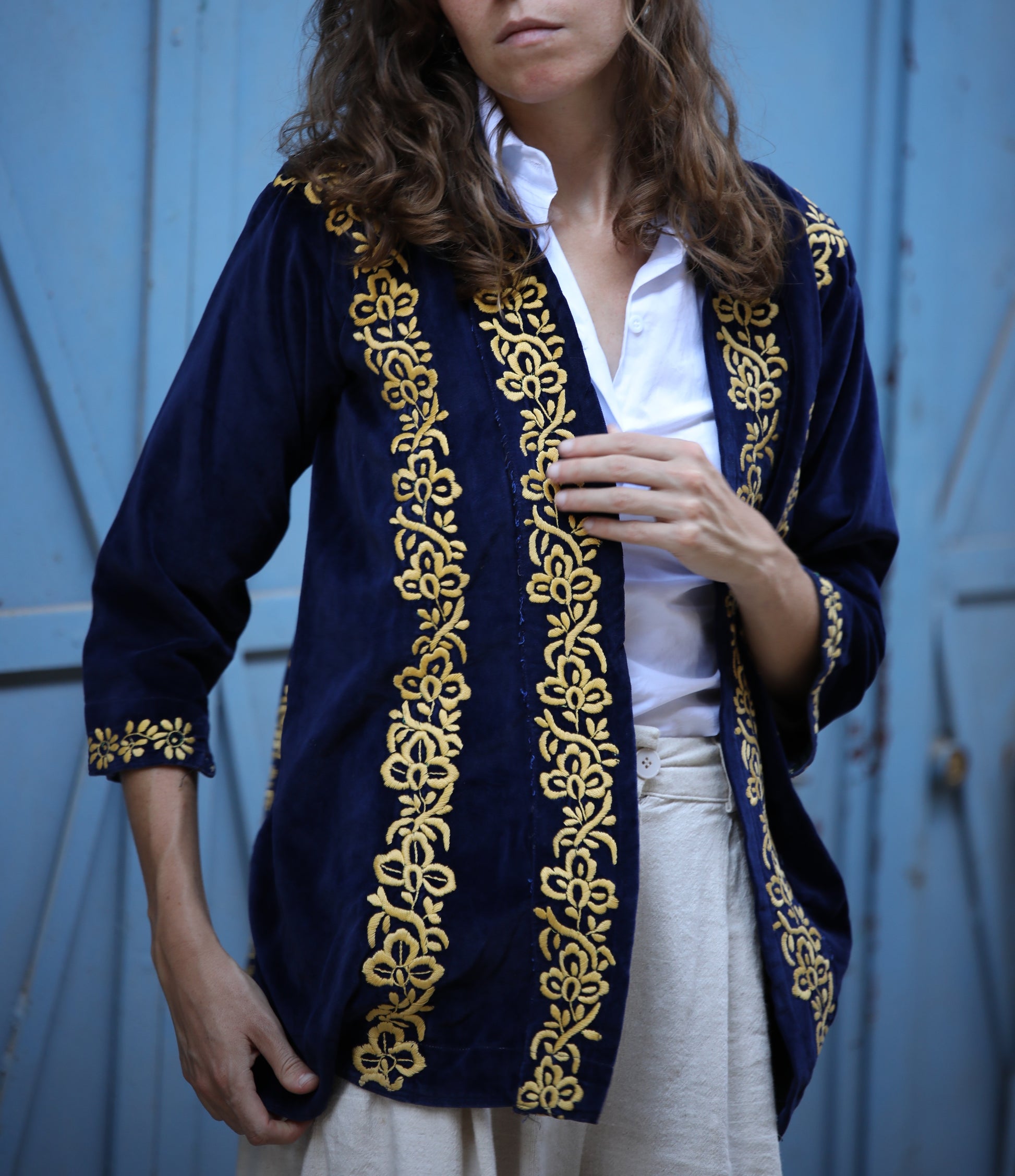 Woman wearing a navy blue cardigan with gold embroidery against a light blue background