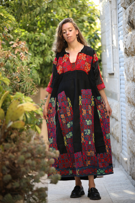 Woman wearing a colorful embroidered dress standing outdoors.