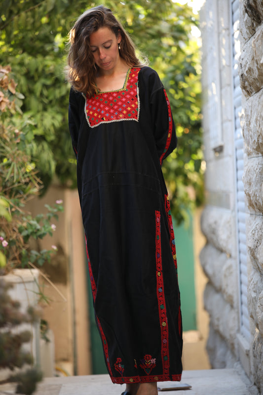 Woman wearing a black dress with red embroidery standing outdoors.