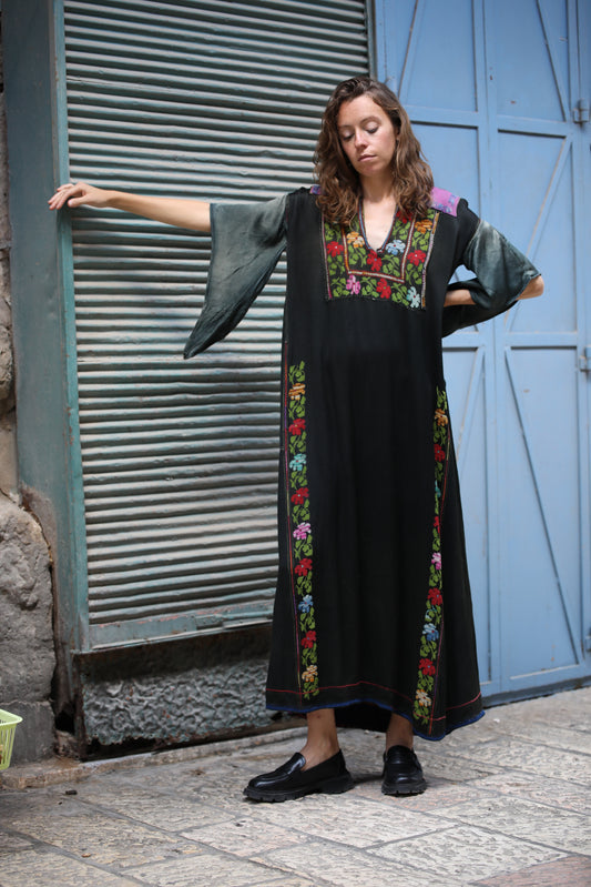 Woman wearing a long, dark dress with floral embroidery standing in front of a blue door.