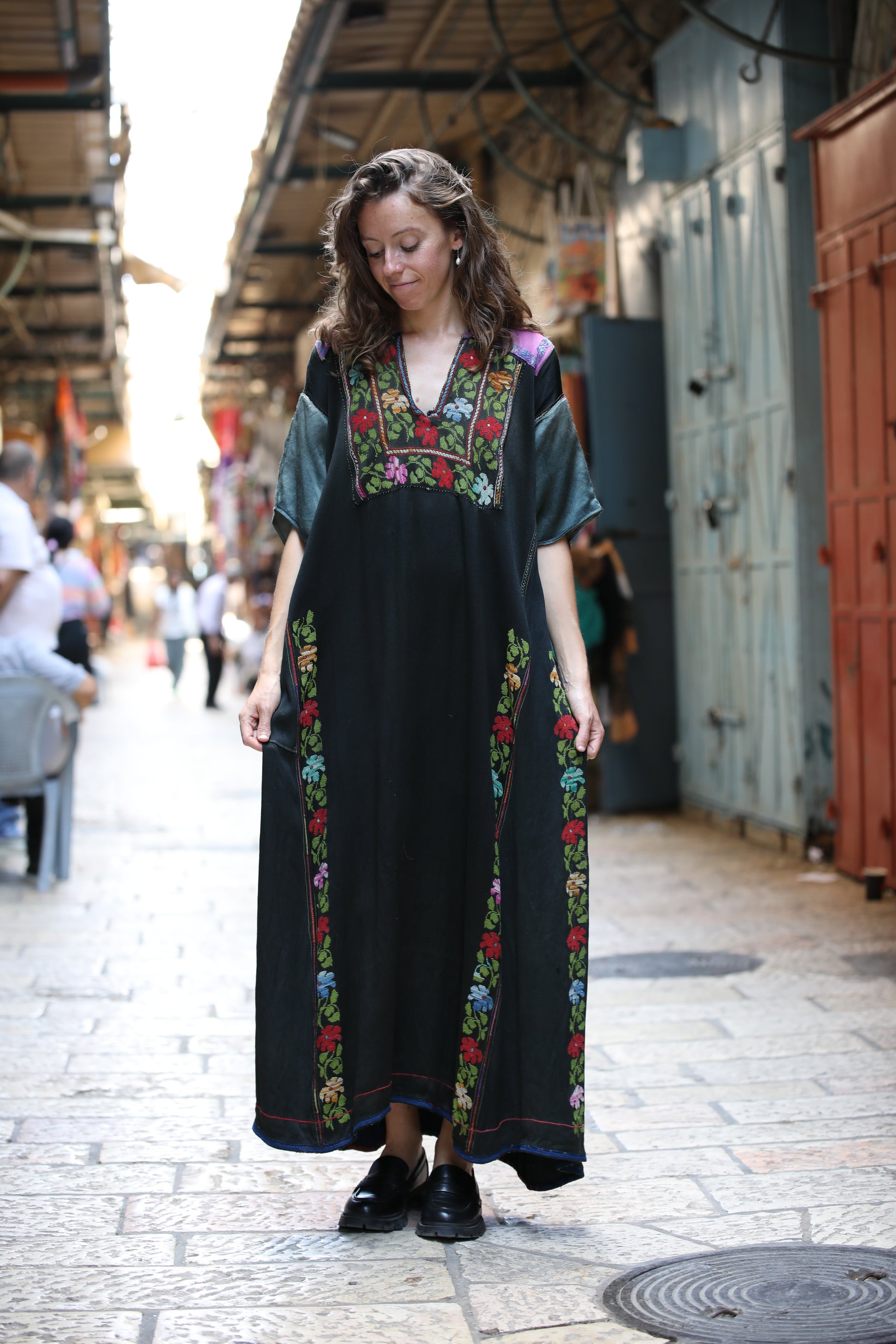 Woman wearing a long black dress with colorful floral embroidery in an urban setting.