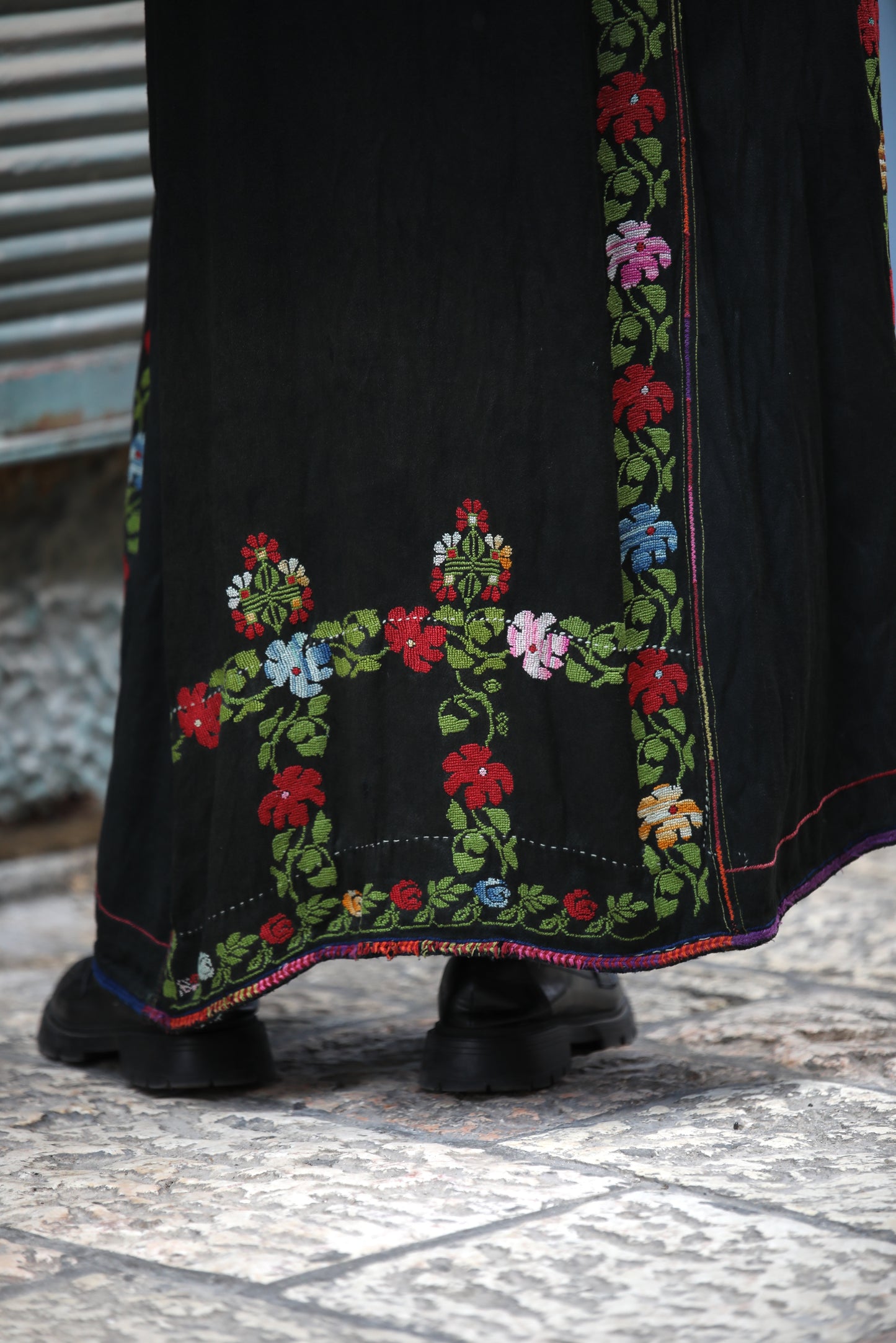 Black dress with colorful floral embroidery on a textured floor.