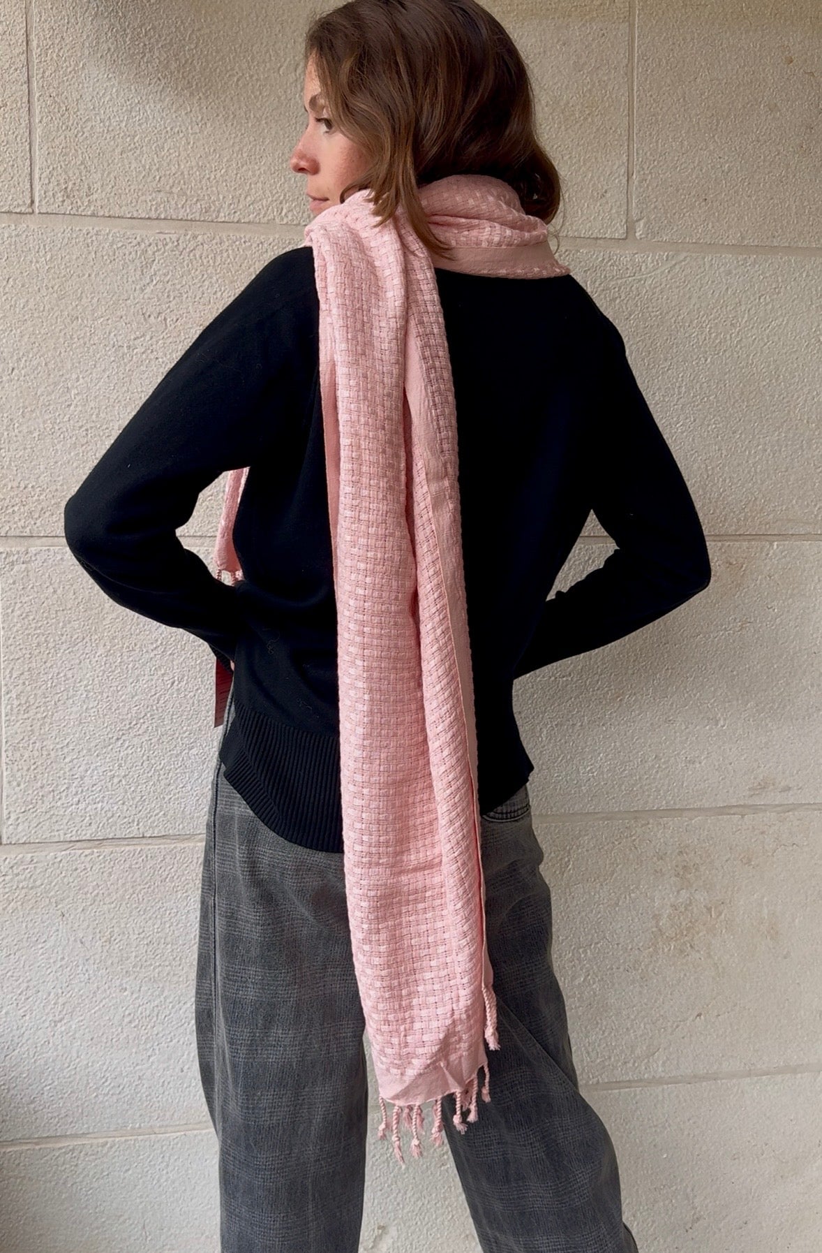 Person wearing a pink scarf against a light stone wall