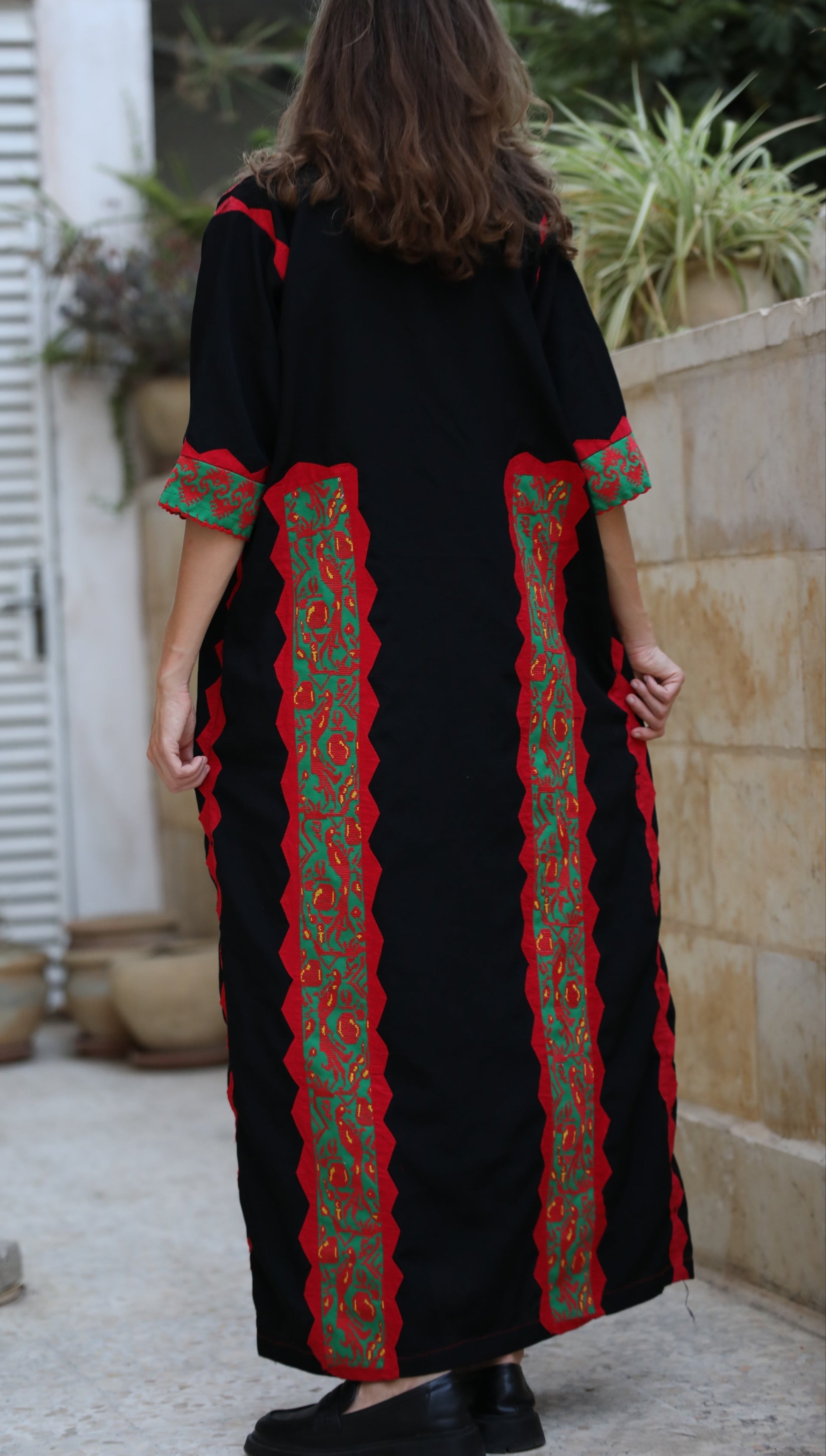 Person wearing a black dress with red and green patterns in an outdoor setting.