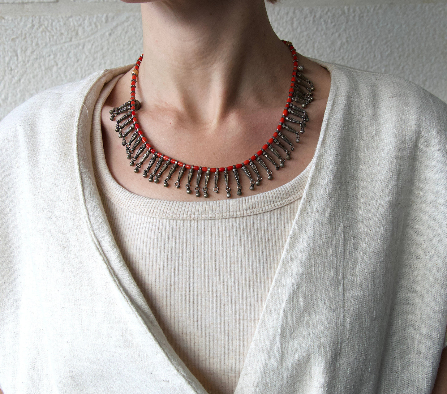 Person wearing a detailed necklace with a plain background