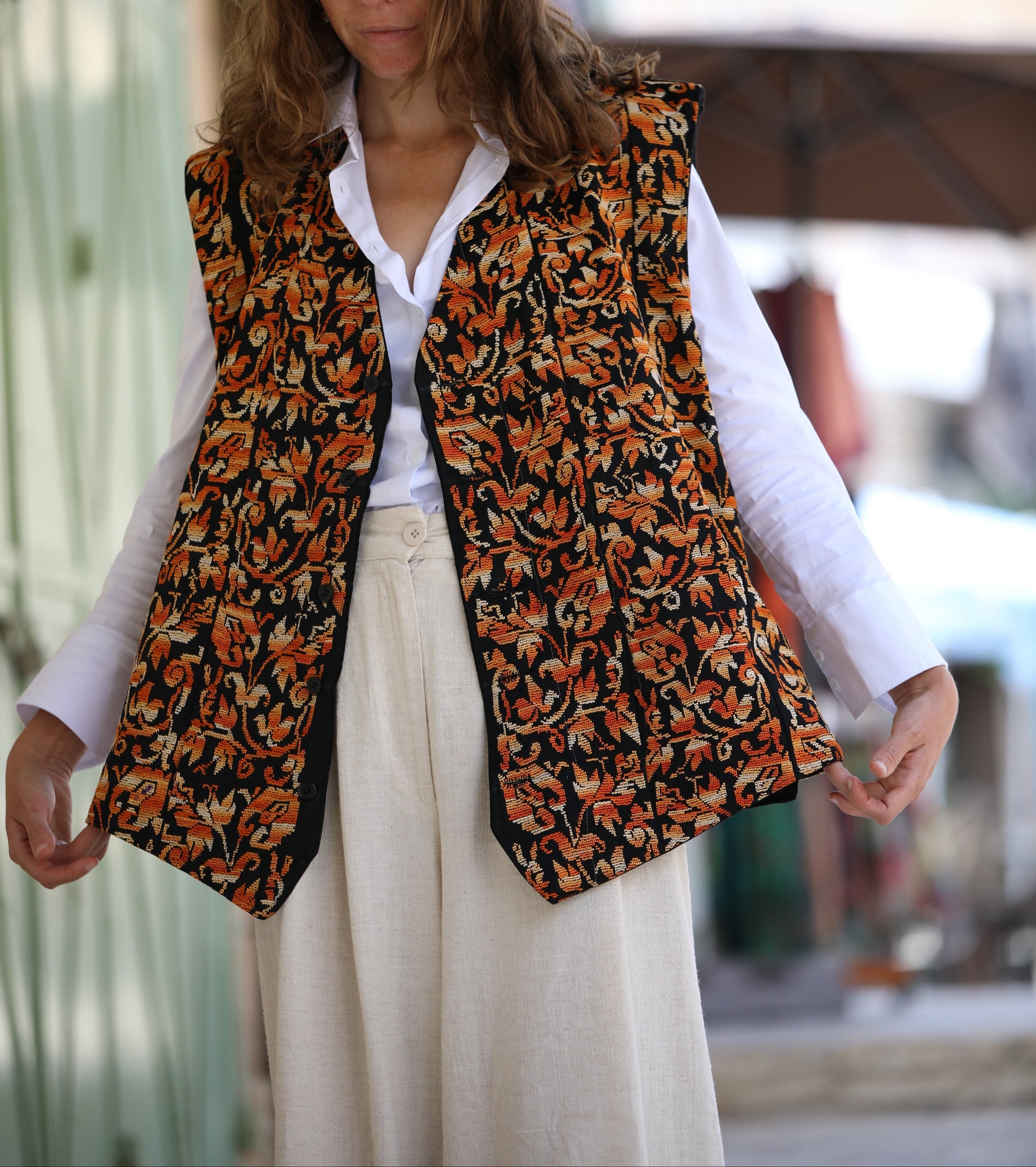 Woman wearing a patterned vest over a white shirt with a blurred background