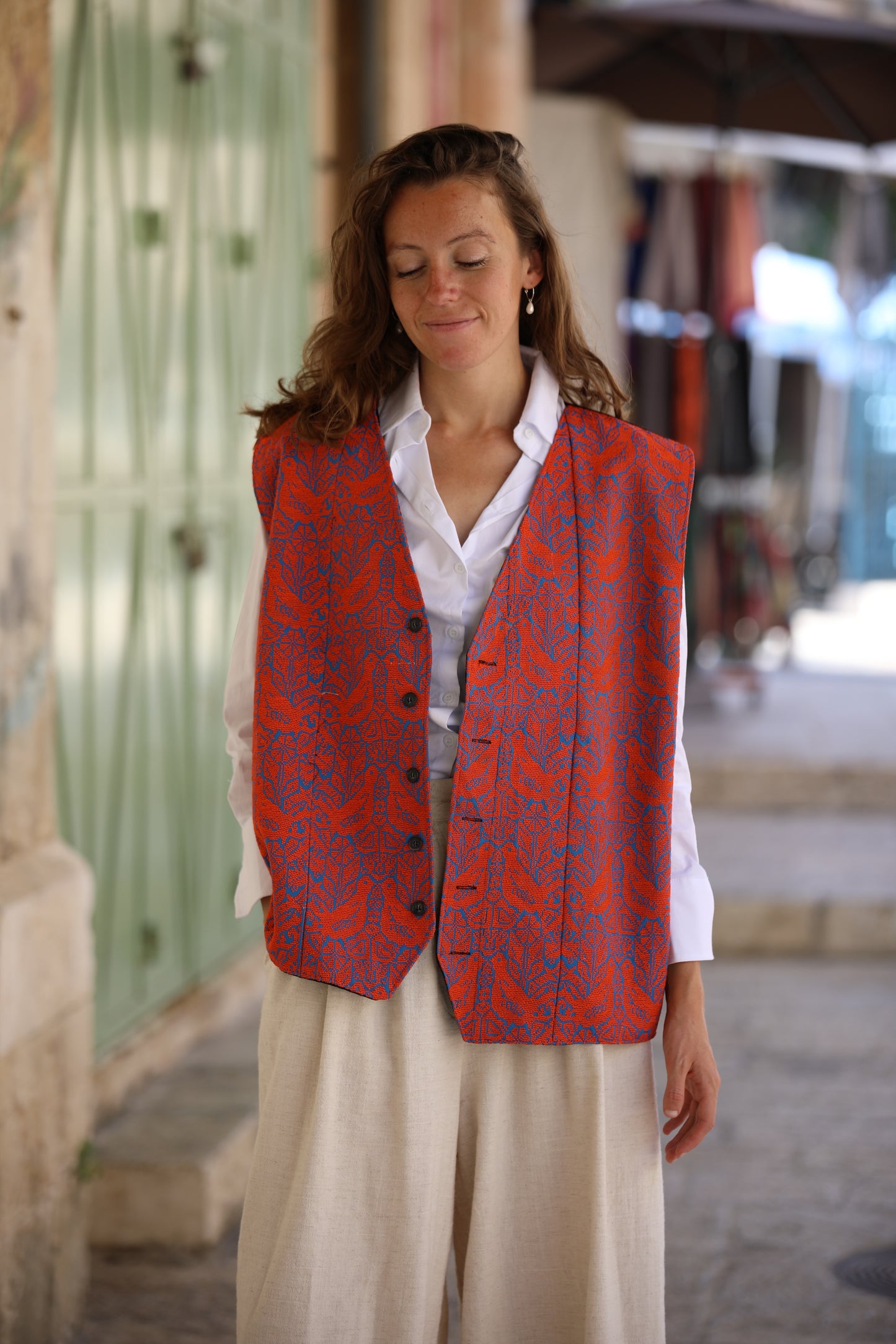 Woman wearing an orange patterned vest over a white shirt in an outdoor setting