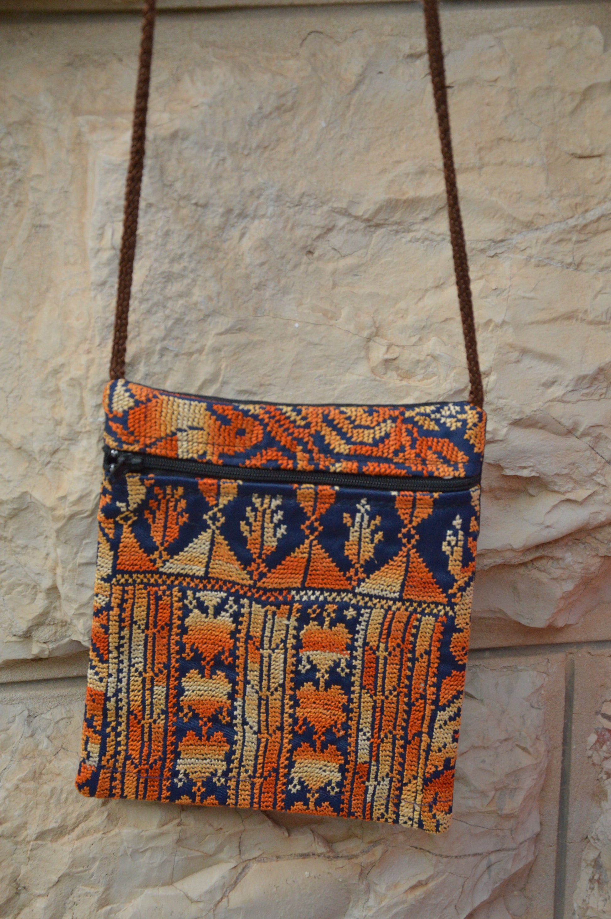 Colorful woven bag with geometric patterns hanging against a stone wall.