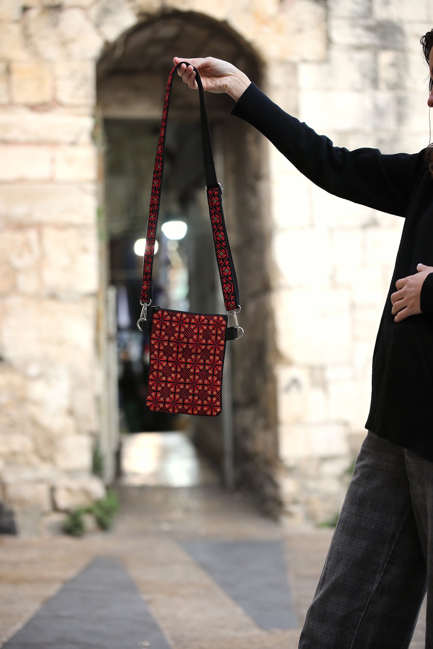 Person holding a red patterned bag in front of a stone archway.